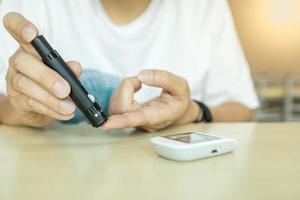 close-up van de handen van de mens met behulp van lancet op de vinger om de bloedsuikerspiegel te controleren met een glucosemeter. gebruik als medicijn, diabetes, glycemie, gezondheidszorg en mensenconcept. foto