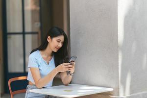 jonge aziatische vrouw die telefoon gebruikt bij een koffiewinkel gelukkig en glimlach. foto