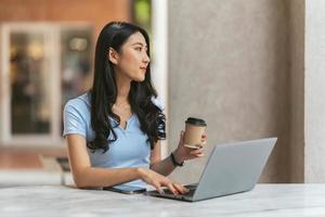 portret van aziatische jonge vrouw die aan laptop en financieel rapport werkt bij coffeeshop. foto