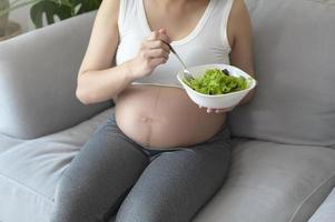 jonge zwangere vrouw met salade thuis, gezondheidszorg en zwangerschapszorg foto