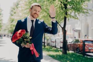 gelukkige mannelijke zakenman in pak met boeket groet iemand in stadspark foto