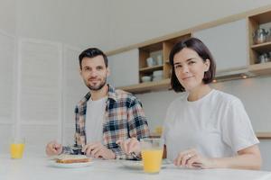 familie en voedingsconcept. man en vrouw kijken vreugdevol naar de camera, genieten van een heerlijk ontbijt, drinken vers gemaakt sap, bespreken hun gezinsplannen, poseren in moderne keuken, gezellige sfeer foto