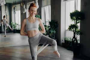 slanke mooie fitnessvrouw met rood haar die beenoefening doet met rubberen weerstandsband foto