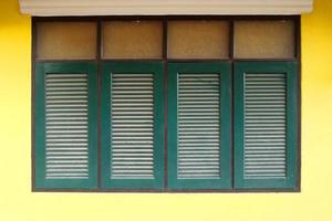 rij retro donkergroene ramen in rechthoekige vorm en felgele muur van huis in thailand. foto