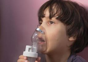 het kind inhaleert, de jongen inhaleert het medicijn door het masker foto