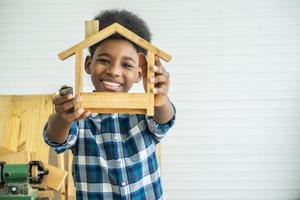 lachende afro-amerikaanse jongenstimmerman kijkt naar zijn eigen houten huis dat zijn vader helpt het graag te doen foto