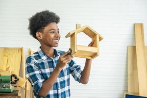 lachende afro-amerikaanse jongenstimmerman kijkt naar zijn eigen houten huis dat zijn vader helpt het graag te doen foto