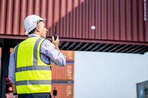 jonge mannelijke ingenieur of manager gebruikt radiocommunicatie om containerlading te regelen in industriële transport- en logistieke concepten. foto