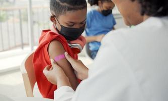 Afro-Amerikaanse arts brengt pleister aan op de schouder van een kind nadat hij is ingeënt. opening mouwen om te vaccineren tegen griep of epidemie in de gezondheidszorg en gevaccineerd concept. foto