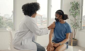 Afro-Amerikaanse arts brengt pleister aan op de schouder van een kind nadat hij is ingeënt. opening mouwen om te vaccineren tegen griep of epidemie in de gezondheidszorg en gevaccineerd concept. foto