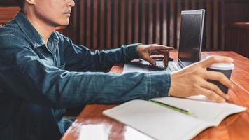 een jonge man met een bril die een laptop gebruikt die op een toetsenbord typt, e-mails schrijft of online werkt op een computer in zijn woonkamer. foto