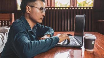 een jonge man met een bril die een laptop gebruikt die op een toetsenbord typt, e-mails schrijft of online werkt op een computer in zijn woonkamer. foto