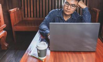 een jonge man met een bril die een laptop gebruikt die op een toetsenbord typt, e-mails schrijft of online werkt op een computer in zijn woonkamer. foto