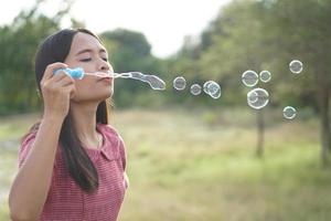 Aziatische vrouw die zeepbellen blaast op elke groene grasachtergrond foto