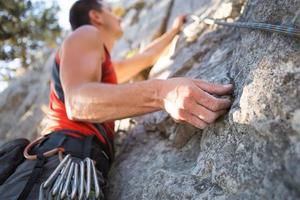 klimmer in rood t-shirt beklimt een grijze rots. een sterke hand greep de leiding, selectieve focus. kracht en uithoudingsvermogen, klimuitrusting touw, harnas, krijt, krijtzak, karabijnhaken, bretels, quickdraws foto