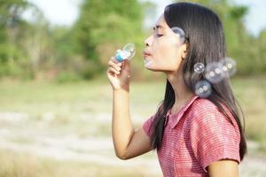 Aziatische vrouw die zeepbellen blaast op elke groene grasachtergrond foto