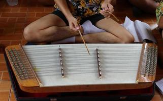 een studentenjongen speelt khim op donkere vloer, thailand. khim is een thais instrument gemaakt van breed hout en snaren, de vorm lijkt op een chinees hakkebord. foto