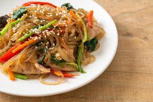 japchae of geroerbakte Koreaanse vermicelli noedels met groenten en varkensvlees gegarneerd met witte sesam foto