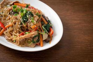 japchae of geroerbakte Koreaanse vermicelli noedels met groenten en varkensvlees gegarneerd met witte sesam foto