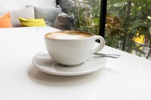 warme koffie op de witte tafel in het café bij de bank en het glazen raam. foto