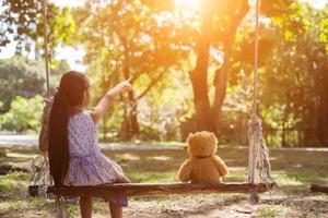 een klein meisje en een teddybeer zittend op een schommel. foto