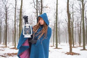 jonge vrouw in retro blauwe jas loopt in het mistige park in de winter, sneeuw en bomen achtergrond, fantasie of sprookjes concept foto