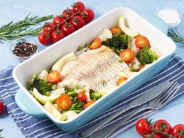 vis kabeljauw gebakken in blauwe oven met groenten - broccoli, tomaten. gezond dieet voedsel. foto
