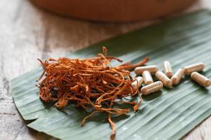 droge cordyceps militaris op een groen bananenblad met houten achtergrond. oranje medische paddenstoel voor een goede gezondheid met capsules. foto