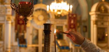 orthodoxe kerk. Christendom. hand van priester die brandende kaarsen aansteekt in de traditionele orthodoxe kerk op paasavond of kerstmis. religie geloof bidden symbool.