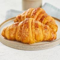 twee heerlijke croissants op bord en warme drank in mok. ochtend Frans ontbijt foto