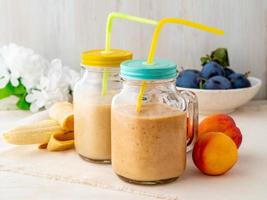 banaan perzik nectarine smoothie in twee potten, vers fruit milkshakes op witte rustieke houten tafel, zijaanzicht foto