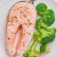 stoom zalm, broccoli, paleo, keto of fodmap dieet. witte plaat op blauwe tafel, bovenaanzicht, close-up foto