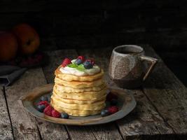 pannenkoek met vanilleroom, bosbessen en frambozen. donkere humeurig oude rustieke houten achtergrond. foto