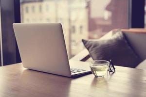 freelance bureau met opengeklapte laptop, kopje groene thee en glazen op tafel foto