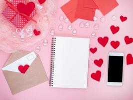 cadeau in rode geschenkdoos met strik, notitieblok, smartphone, envelop, kaart, rood hart, roze achtergrond, plat leggen, kopieer ruimte foto