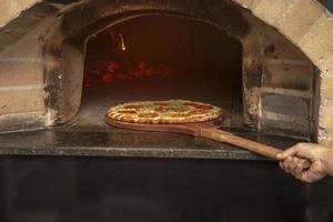Braziliaanse pizza wordt gekookt in een houtgestookte oven. pizza koken in een traditionele bakstenen houtoven. steenoven pizza op de houten houder gaat bakken. foto