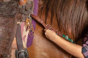 vrouw zadelt een paard en spant de singel aan. voorgrond. foto