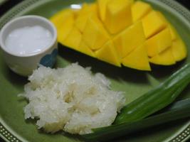 mango plakkerige rijst met kokosmelk, zoet voedseldessert op groene plaat, barracuda mango geel fruit foto