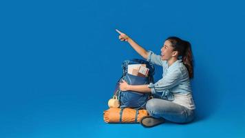 jonge Aziatische reiziger gelukkige vrouw in blauw shirt met rugzak met en uitrusting voor reizigers vakantie met een kaart, op blauwe kleur achtergrond. reis rugzak foto