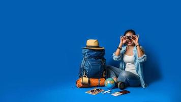 jonge Aziatische reiziger gelukkige vrouw in blauw shirt met rugzak met en uitrusting voor reizigers vakantie met een kaart, op blauwe kleur achtergrond. reis rugzak foto