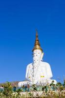 weids uitzicht een groot wit boeddhabeeld achter een berg en een blauwe lucht in wat pha son kaew, khao kho district, phetchabun provincie, thailand foto