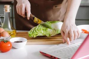 vrouw bereidt thuis een groentesalade met een videorecept. online koken, met behulp van laptop in de keuken. foto