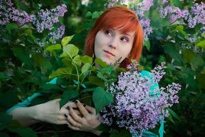 jonge vrouw met boeket van seringen in het voorjaar. roodharige dame snuift paarse bloemen. portret van aantrekkelijke vrouw in bloementuin. foto