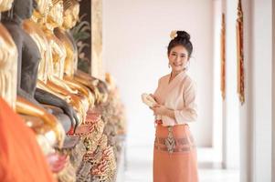 Thaise mooie vrouwen in traditionele Thaise kleding gebruiken verse bloemenslingers om hulde te brengen aan het boeddhabeeld, om een wens te doen op het Thaise Songkran-festival foto