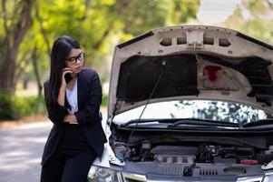 een jonge Aziatische vrouw belt haar servicemonteur om een kapotte auto aan de kant van de weg te repareren foto