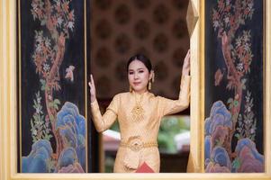 een mooie, sierlijke Thaise vrouw in Thaise jurk versierd met waardevolle sieraden staat in een prachtige oude Thaise tempel foto