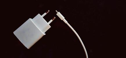 witte smartphone-oplader op de zwarte achtergrond. smartphone opladen elektronisch apparaat. foto