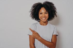 mooie zwarte vrouw vrolijk met een stralende glimlach op haar gezicht wijzend met hand en vinger omhoog foto