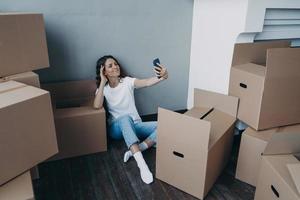 gelukkige vrouw dozen uitpakken en selfie nemen in nieuw luxe appartement. succesconcept. foto