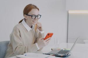 lachende jonge vrouw sms't op het werk of in de klas. meisje wordt afgeleid op het werk op kantoor. foto